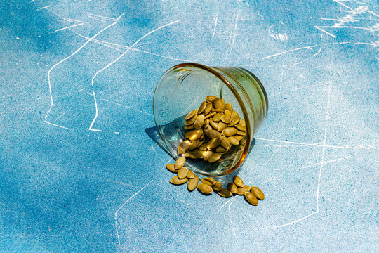 Pumpkin seed spilling from glass on blue textured background
