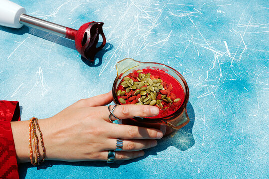 Hand holding healthy beetroot soup bowl with seed and blender