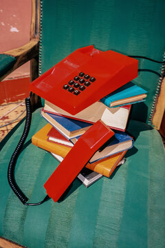 Red retro landline telephone on a stack of books on a green chair