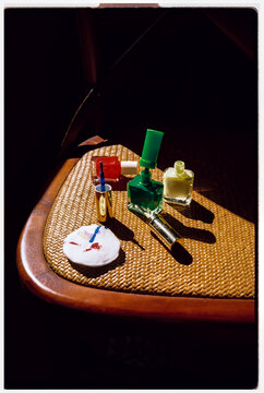 Colorful nail polish bottles sit on a woven chair in bright sunlight