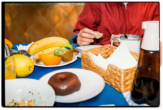 A breakfast table features fresh fruit and a chocolate donut indoors