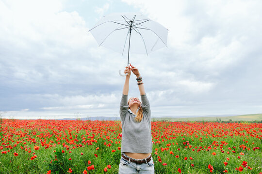 Carefree woman raises a white umbrella in a red poppy field