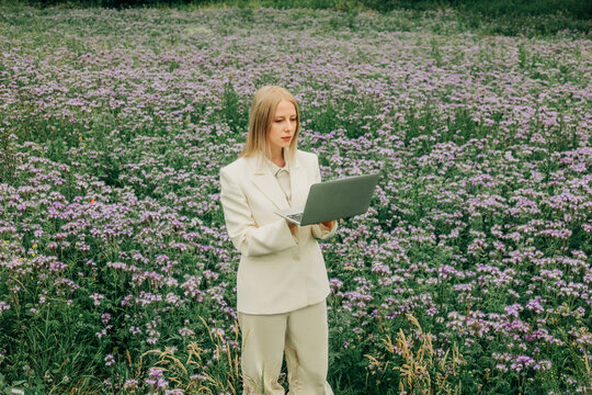 Businesswoman works on a laptop in a summer meadow of phacelia