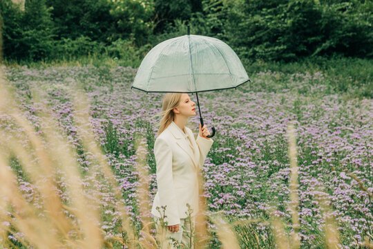 Woman in white suit holds umbrella in a summer phacelia meadow