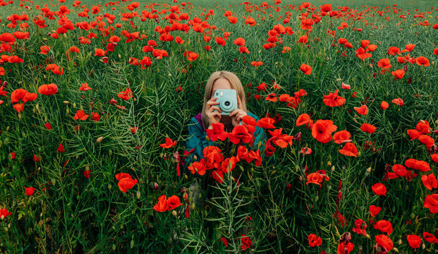 Woman takes a photograph with a vintage camera in a poppy field