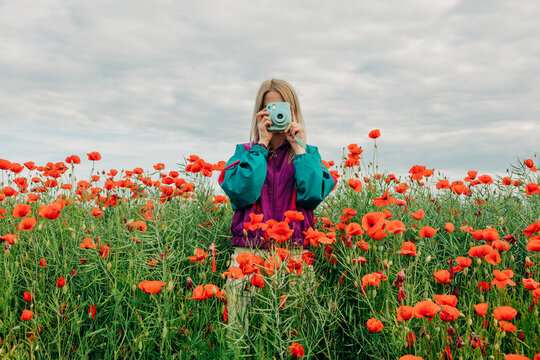 Woman in tracksuit photographs poppy meadow with vintage camera