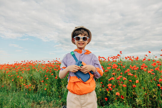 Smiling boy in retro tracksuit standing in a blooming poppy meadow