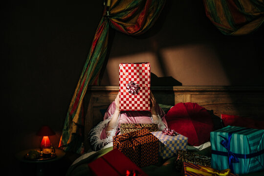 Woman in bed hides her face behind a large wrapped birthday gift