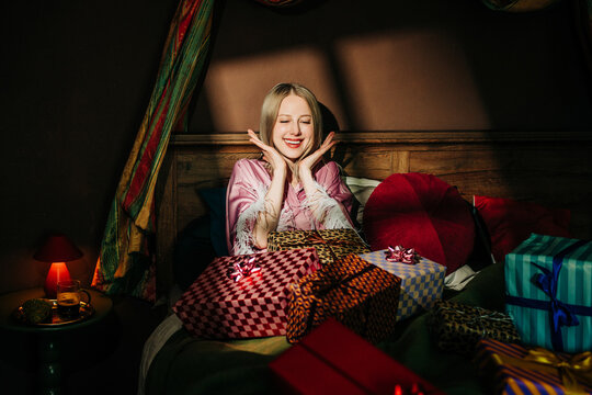 Smiling woman finds birthday gifts in bed in the morning