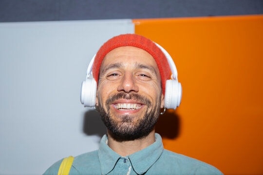 Smiling man in beanie listens to music on headphone in Barcelona