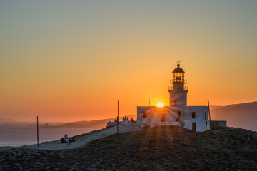 Armenistis Lighthouse on Mykonos at sunset with the sun setting over the Aegean Sea and a path leading up the hill, Cyclades, Greece © Michal Plevko