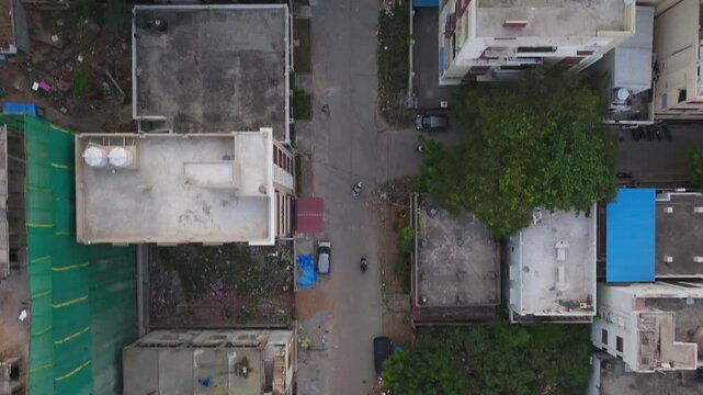 Bird eye view of Vehicle moving on narrow road with buildings terrace and parked vehicles at puppalaguda, manikonda, hyderabad, telangana, india. day time, push in shot, drone shot, 4k.