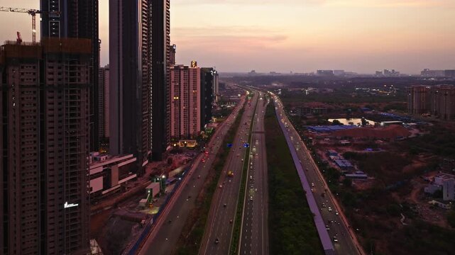 8 lane road of Nehru ORR with service road, vehicles, tower buildings and orange sky at Kokapet, financial district, Narsingi, hyderabad, telangana, india. sun set time, push in shot, drone shot, 4k.