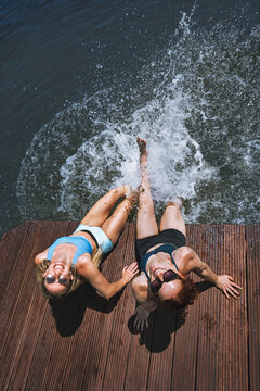 A shot of two attractive young women in bikinis at a small lake, standing in the water right by the shore - capturing the concept of having fun and cooling off during summer vacation.