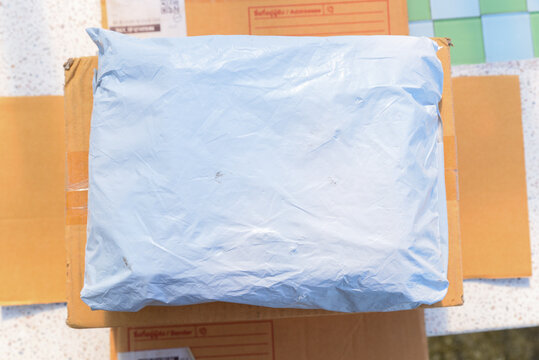 Packaged parcel wrapped in light blue plastic on top of cardboard boxes on table