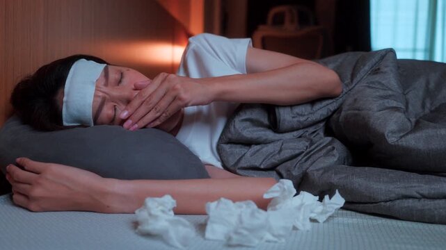 Pile of used tissues near a sleeping ill Asian female with a fever patch. Concept of seasonal virus, health symptoms, and nighttime rest for recovery at home.