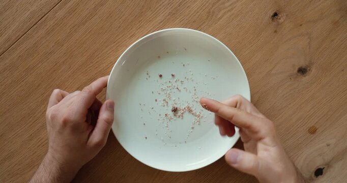 Top view of a person picking up and eating the last crumbs from a plate with a finger. Concept of hunger, food waste, satisfaction, and everyday eating.