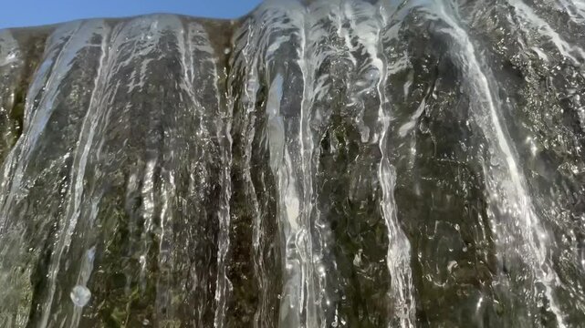 Artificial concrete check dam directs water into churning, frothy river stream lined with green trees