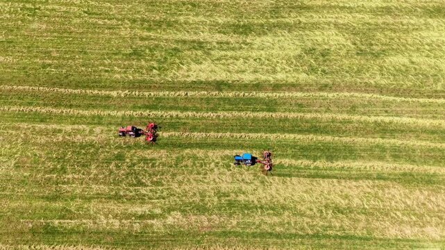 Tractors preparing fields with parallel lines of freshly cut grass in the summer sun, aerial view