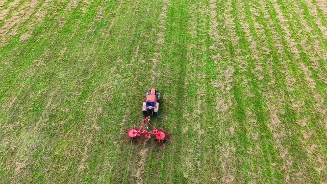 Tractor tilling fertile green field with patterned rows of freshly cut grass and soil