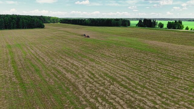 Tractors cutting grass in expansive green field during clear sunny day with few clouds, aerial view