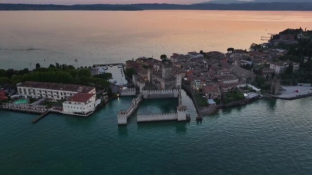 Sirmione, Italy - 4K Flying towards Scaligero Castle (Castello Scaligero di Sirmione) at the comune of Sirmione, located at the lower part of Lake Garda. Sunset, dramatic golden sky and clouds