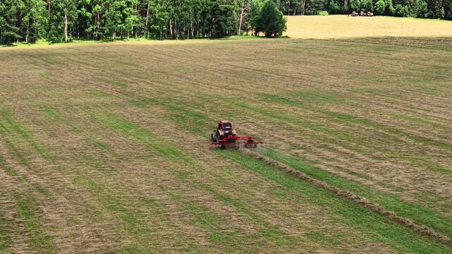 Spreading fresh cut hay in open fields creates lush green textures under bright sunlight, aerial view