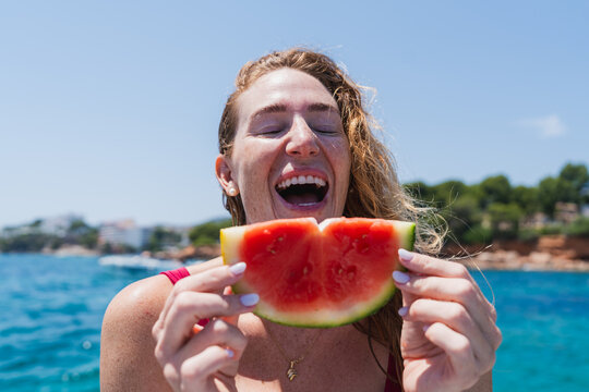 Laughing woman holding watermelon slice on summer beach vacation