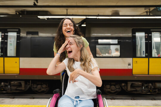 A woman pushes her laughing friend in a wheelchair at the metro