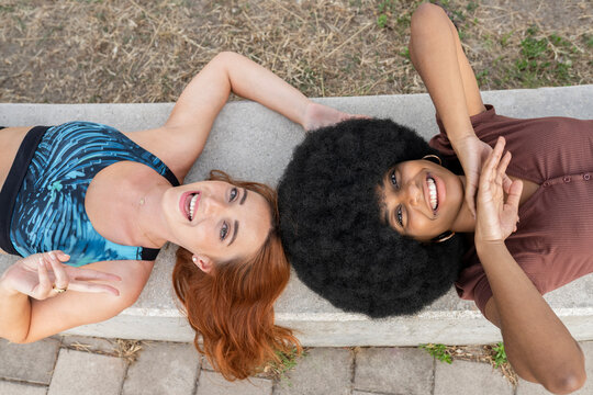Redhead woman gesturing while lying with female friend on bench