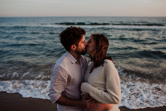 Expecting couple kissing on the beach at sunset
