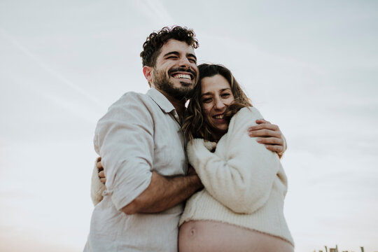 Smiling expecting couple hugging outdoors