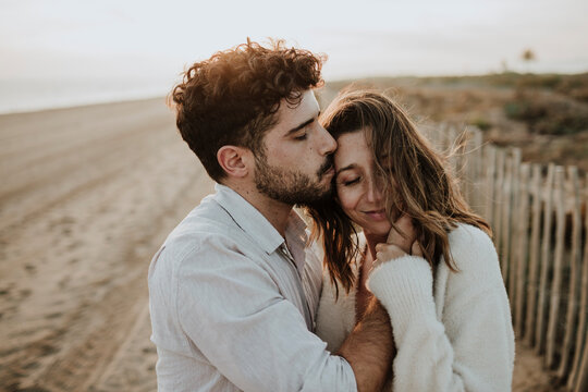 Affectionate expecting couple sharing a kiss on the beach at sunset