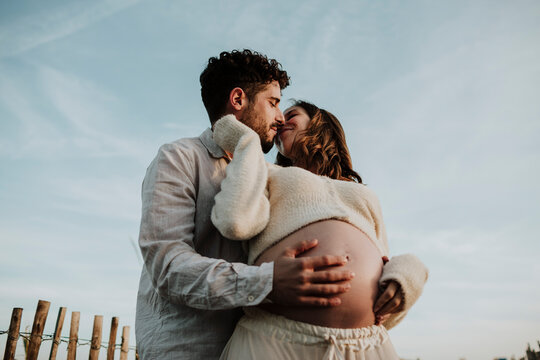 Expecting man and woman embracing outdoors touching pregnant belly