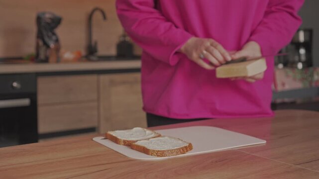 A woman's hands slice cheese for sandwiches with a knife.