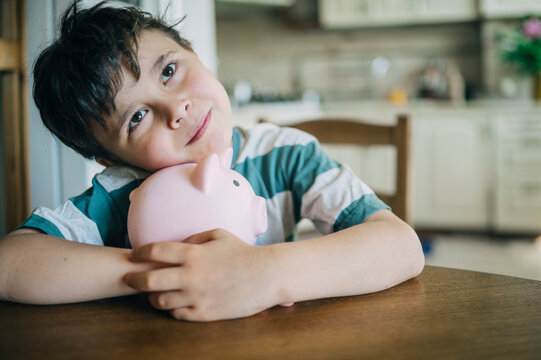 Boy hugs a pink piggy bank at home while dreaming about the future