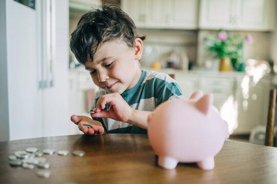 A boy puts money into a piggy bank on a kitchen table