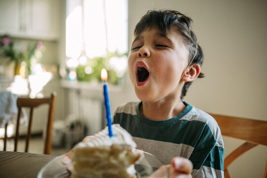 A young boy blows out a candle on his birthday cake indoors
