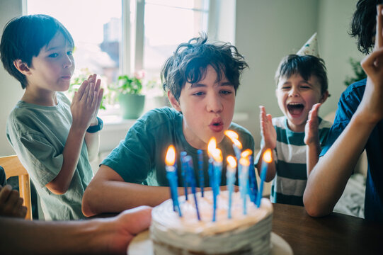 Teenager blows out birthday candles while boys clap indoors