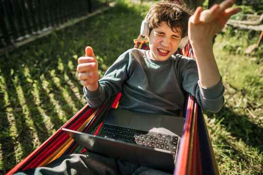 Angry boy plays video game on laptop in hammock outdoors