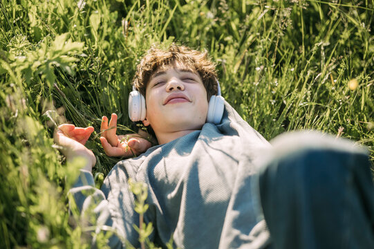 A teenage boy enjoys music while lying on the summer grass
