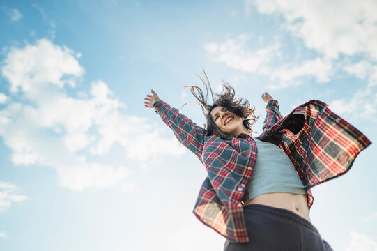 Happy woman raises her arms outdoors enjoying the wind