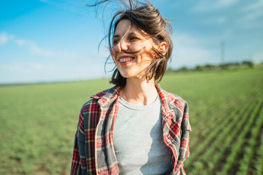 Smiling woman stands in a green agricultural field enjoying the wind