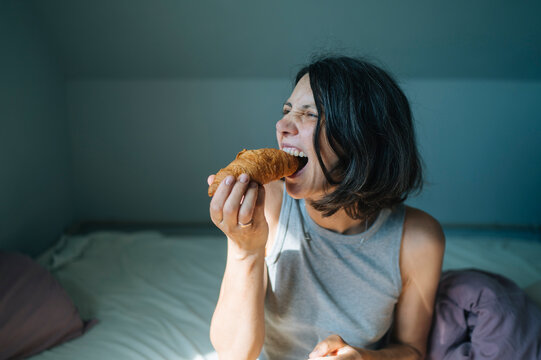 Woman eating a delicious croissant for breakfast in bed at home
