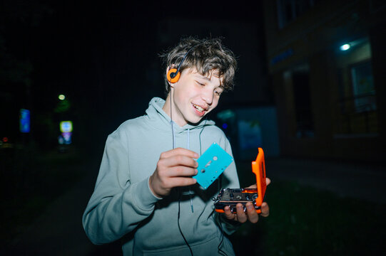 Smiling teenager walking at night holding a retro cassette tape