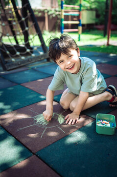 Smiling boy drawing a sun with chalk on a playground in summer