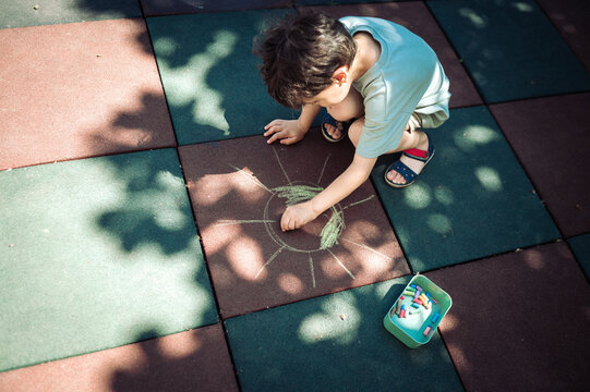 Boy crouches on a playground drawing a sun with chalk