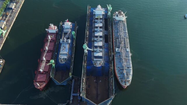 commercial cargo ships and heavy oil tankers undergoing essential maintenance and structural repairs inside floating dry docks at a busy industrial shipyard marine facility.