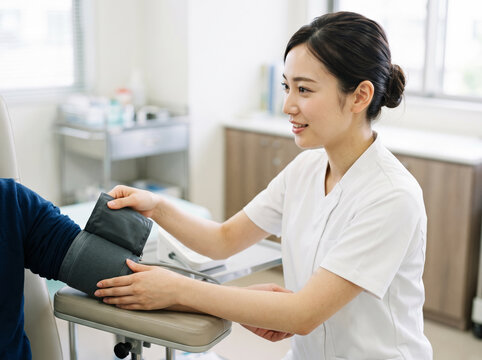 処置室で患者の腕に血圧計を装着して丁寧にケアをする看護師の女性