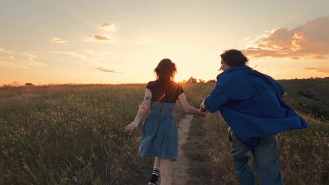 Young couple running hand in hand across meadow at golden sunset. Concept of romantic getaway, youthful freedom, summer adventure, weekend escape and happy relationship.
